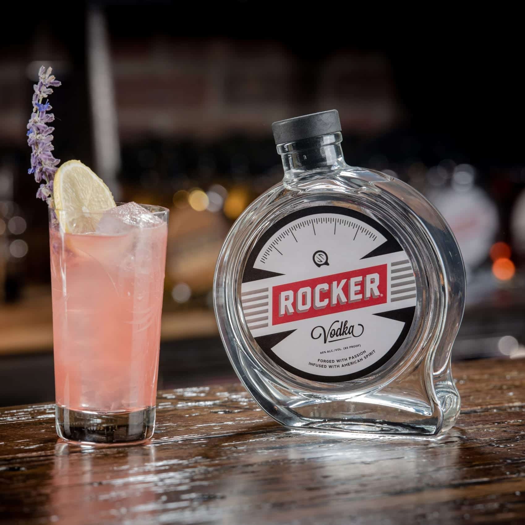 Custom labeled Rocker Vodka bottle and nicely decorated pink cocktail on a wooden counter.