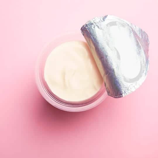 Opened cosmetic cream container on a pink surface.