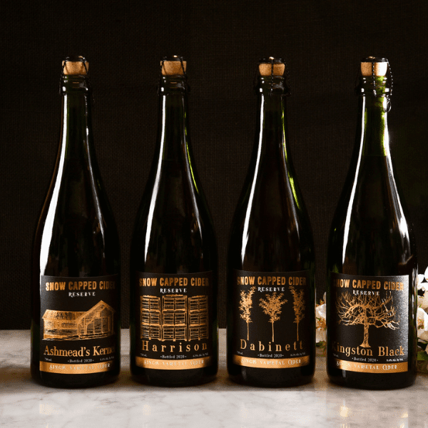 Four black bottles of Snow Capped Cider featuring embossed hot stamp stylish custom labels made by a professional labeling company from Denver.